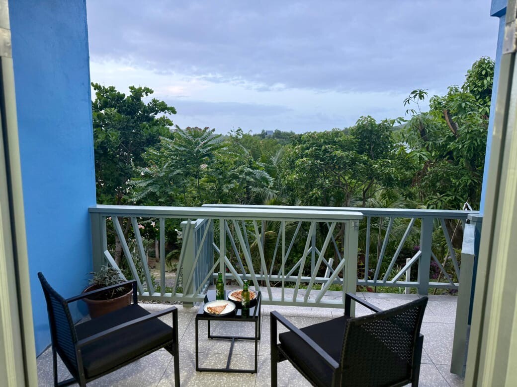 Balcony with coffee table and 2 chairs overlooking lush trees 