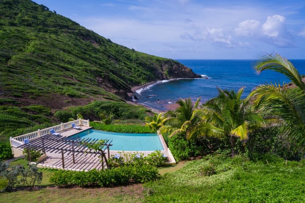 Pool and patio surrounded by lush greenery overlooking the sea 